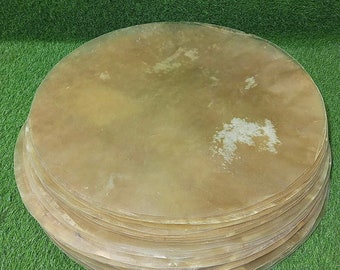 May include: A stack of round, light brown leather drumheads. The drumheads are stacked on top of each other, with the top one being slightly larger than the others.