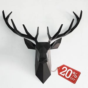 Op de afbeelding: Zwarte geometrische hertenkop wanddecoratie met grote geweien. De hertenkop is aan een witte muur bevestigd. Een rood label met "20% OFF" is bevestigd.