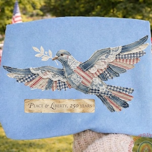May include: A light blue fabric item featuring a dove design with denim, lace, and red, white, and blue fabric accents. The dove holds an olive branch. Text on the item reads "Peace & Liberty, 250 years."