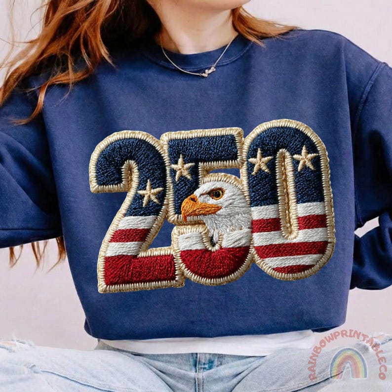 K&ouml;nnte beinhalten: Marineblaues Sweatshirt mit einem gestickten Design. Das Design zeigt die Zahl "250", einen Adler und die Farben der amerikanischen Flagge. Es enth&auml;lt rote und wei&szlig;e Streifen, Blau mit wei&szlig;en Sternen und einen Adlerkopf.