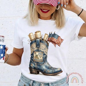 May include: White t-shirt featuring a distressed blue cowboy boot graphic. The boot is filled with rolled scrolls and American flags. The boot has a patch that reads "250 Years of Freedom".