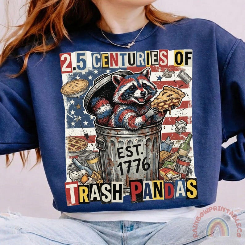 May include: Navy blue sweatshirt with a graphic of a raccoon in a trash can, holding pie. The design includes the text "2.5 Centuries of Trash Pandas" and "Est. 1776" with an American flag background.