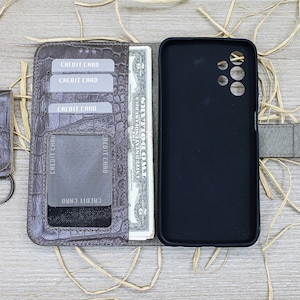 May include: A gray leather wallet case with a phone case, three credit card slots, a cash slot, and a key chain. The case has a crocodile pattern.