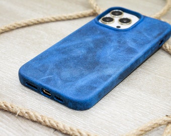 May include: A blue leather phone case with a distressed finish. The case has a raised edge around the camera and a cutout for the charging port. A rope is in the background.
