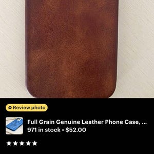 May include: A brown full-grain leather phone case. The case has a textured surface and a camera cutout. The phone case is designed to protect the phone from scratches and damage.