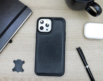 May include: A black leather phone case with a stitched border, next to a black notebook, pen, and a pair of white wireless earbuds. A small piece of black leather is also present. The items are on a light wood-grain surface.