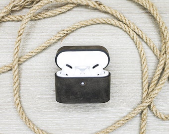 May include: A black leather case for wireless earbuds, open to reveal the white earbuds inside. The case is sitting on a light wood surface with a brown rope coiled around it.