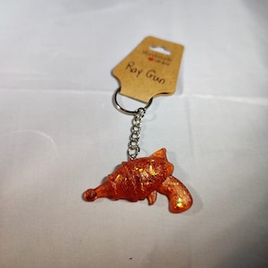 May include: Orange glitter ray gun keychain with a silver chain and a brown tag that says "Handmade with love" and "Ray Gun".