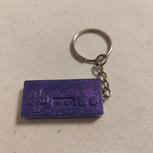 May include: A blue and purple glitter keychain shaped like a retro video game controller.