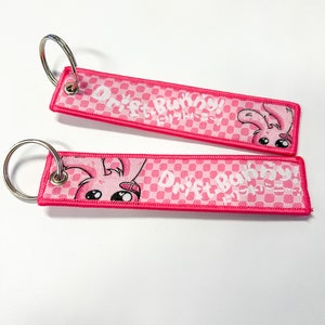 May include: Two pink fabric keychains with silver key rings. Each keychain has a pink and white checkered pattern with the words "Drift Bunny!" and a cartoon bunny illustration. The edges are a darker pink.