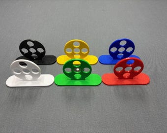 Puede incluir: Una colección de pequeños objetos decorativos abstractos y coloridos. Cada objeto tiene una base rectangular plana y una parte superior circular con cinco agujeros. Los colores incluyen negro, blanco, amarillo, verde, azul y rojo.