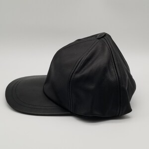 K&ouml;nnte beinhalten: Eine schwarze Baseballkappe aus Leder mit einem gebogenen Schirm. Die Kappe hat ein klassisches Design und ist aus hochwertigem Leder gefertigt.