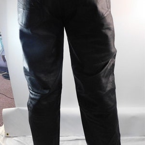 May include: Black leather pants with a classic five-pocket design. The pants have decorative stitching on the back pockets and silver-toned rivets. The leather appears to be soft and has a slight sheen.