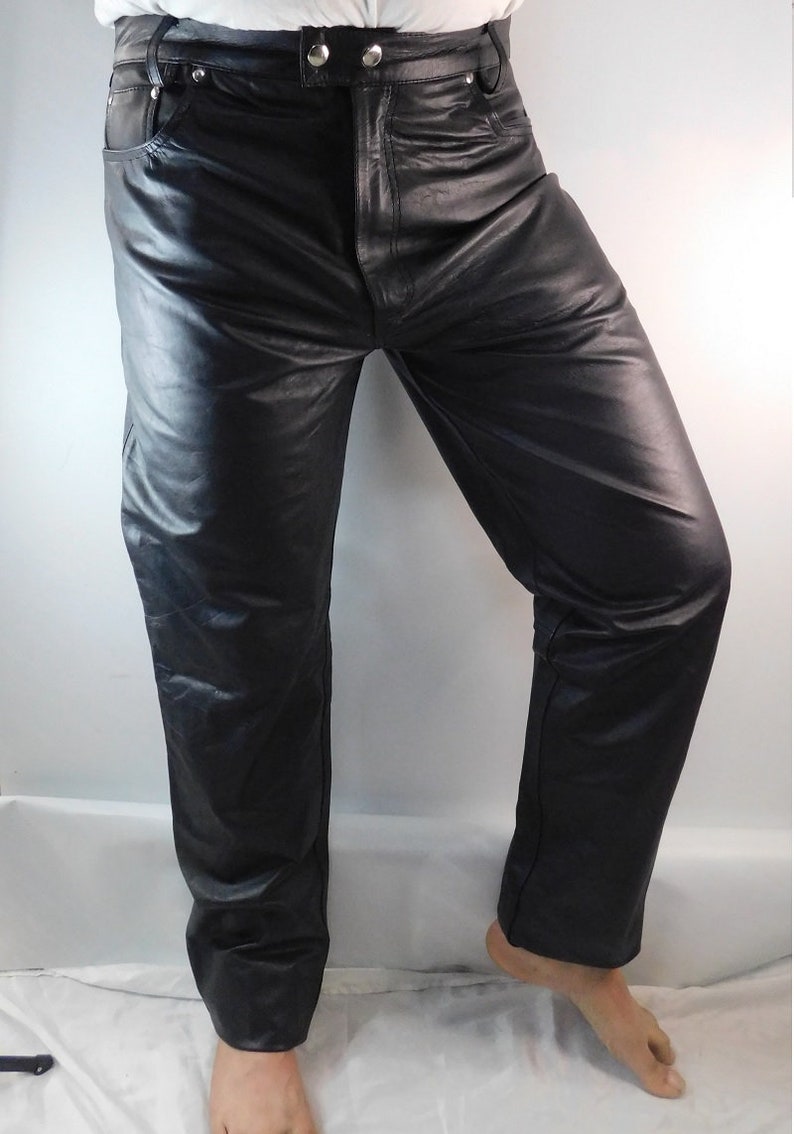 May include: Black leather pants with a classic five-pocket design. The pants have a straight leg cut and a button and zipper closure. The leather appears to be smooth and has a slight sheen. The pants are shown from the waist down.