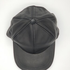 K&ouml;nnte beinhalten: Eine schwarze Leder-Baseballkappe mit einem gebogenen Schirm. Die Kappe hat ein klassisches Design mit einer sechsteiligen Konstruktion und einer gen&auml;hten Naht um den Schirm.