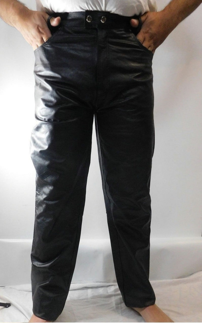 May include: Black leather pants with a high waist and two button closure. The pants have front pockets and a straight leg design. The material has a slight sheen.