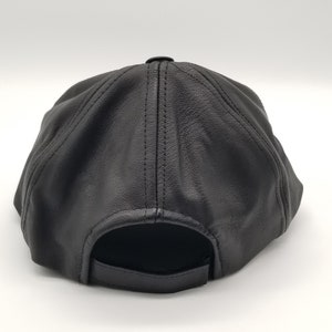 K&ouml;nnte beinhalten: Schwarze Baseballkappe aus Leder mit einem gebogenen Schirm und einem gesteppten Design. Die Kappe hat einen verstellbaren Riemen an der R&uuml;ckseite.