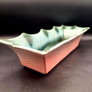 May include: Rectangular ceramic planter with a light pink wood grain pattern on the exterior. The interior is a blend of green and blue hues. The rim has a wavy design.