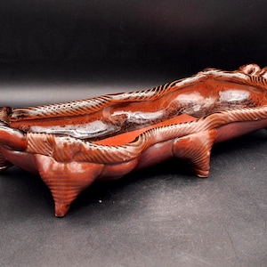 May include: A brown ceramic serving dish with a textured, wavy design. The dish has four legs and is perfect for serving snacks or appetizers.