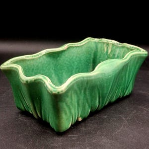 May include: A rectangular, green ceramic planter with a wavy rim. The planter has a textured surface and a glossy finish. The interior is a lighter shade of green. The planter is suitable for small plants or succulents.