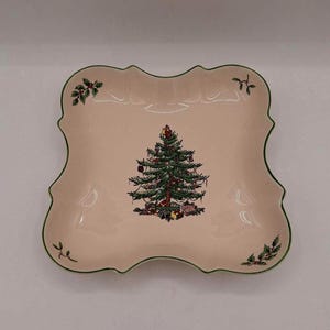 May include: A pink ceramic serving dish with a green scalloped edge. The dish features a Christmas tree design with green, red, and brown accents.