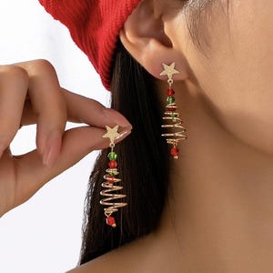 Könnte beinhalten: Goldfarbene Weihnachtsbaum-Ohrringe mit Sternakzenten. Die Ohrringe haben ein Spiraldesign mit roten und grünen Perlen, wodurch ein festlicher Look entsteht. Die Ohrringe sind so konzipiert, dass sie baumeln und das Licht einfangen.