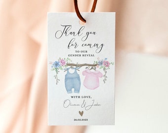 May include: A white card with a thank you message for coming to a gender reveal party. The card features a watercolour illustration of two baby clothes hanging on a clothesline with flowers. The text reads "Thank you for coming to our gender reveal. With love, Olivia & John 26.02.2023"