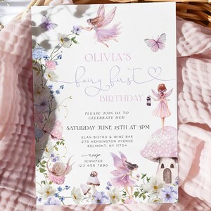 Puede incluir: Una invitación de cumpleaños con temática de hadas con el texto "Olivia's fairy first birthday". La invitación presenta ilustraciones de hadas, mariposas y flores en tonos rosas, morados y azules. Se encuentra sobre una cesta tejida con una tela rosa.