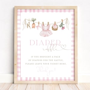 May include: A framed sign with a pink gingham border. The sign reads "DIAPER raffle" with watercolor illustrations of baby clothes and flowers. The text below says "If you brought a pack of diapers for the raffle, please leave your ticket here."