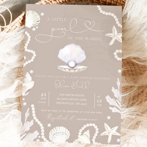 Może przedstawiać: Zaproszenie na baby shower z motywem muszli. Zaproszenie ma jasnobrązowe tło z ilustracjami muszli i pereł. Tekst zawiera "A Little Pearl in the Making" oraz szczegóły wydarzenia.