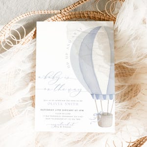Könnte beinhalten: Eine Babyparty-Einladung mit einem Aquarell-Heißluftballon-Design in Blautönen. Der Text "Up Up and Away" und "a baby is on the way" sind zu sehen. Die Einladung enthält Eventdetails und ist vor einem weichen, neutralen Hintergrund.