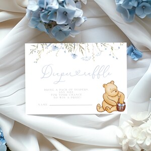Pu&ograve; includere: Un biglietto bianco con disegni floreali blu e un'illustrazione di Winnie the Pooh. Il biglietto dice "Diaper Raffle" e "Porta un pacchetto di pannolini di qualsiasi taglia per avere la possibilit&agrave; di vincere un premio".