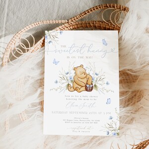 Pu&ograve; includere: Un invito a un baby shower con un'illustrazione ad acquerello di Winnie the Pooh che tiene un cestino di miele. L'invito &egrave; decorato con farfalle blu e fiori. Il testo sull'invito recita "Il miele pi&ugrave; dolce &egrave; in arrivo!" e include la data e l'ora della doccia.