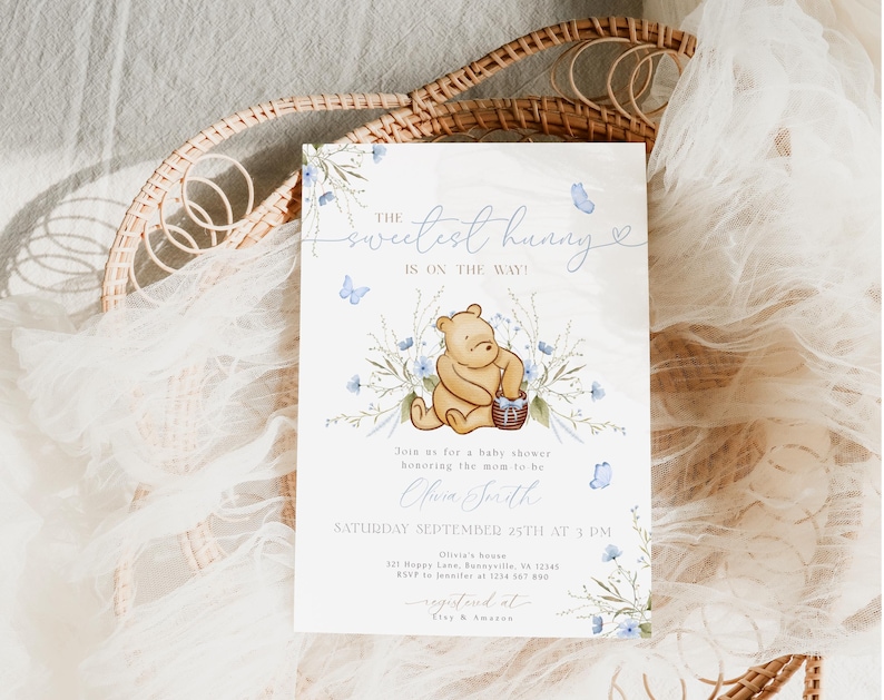 Pu&ograve; includere: Un invito a un baby shower con un'illustrazione ad acquerello di Winnie the Pooh che tiene un cestino di miele. L'invito &egrave; decorato con farfalle blu e fiori. Il testo sull'invito recita "Il miele pi&ugrave; dolce &egrave; in arrivo!" e include la data e l'ora della doccia.