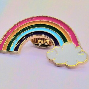 May include: A gold-tone rainbow enamel pin with a white cloud. The rainbow has red, orange, yellow, green, blue, indigo, and violet stripes.