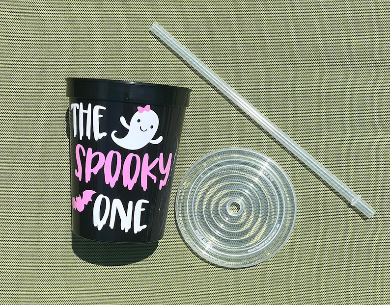 May include: Black reusable cup with a white ghost and the text "The Spooky One" in pink. The cup comes with a clear lid and a clear straw.