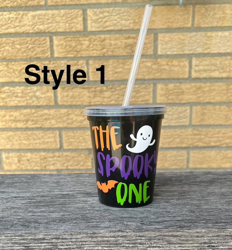 May include: Black plastic cup with a clear plastic straw. The cup has a design that says "The Spooky One" with a ghost, bat, and dripping green and orange paint.