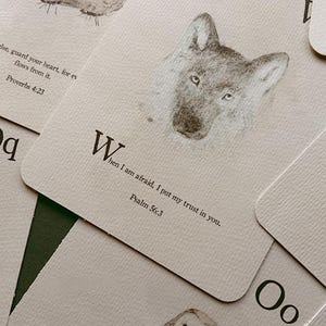 May include: A set of off-white rectangular cards featuring black ink illustrations of a wolf, an owl, and a rock. Each card displays a letter of the alphabet and a Bible verse, including Psalm 98:4, Proverbs 4:23, and Psalm 56:3, with the text When I am afraid, I put my trust in you.