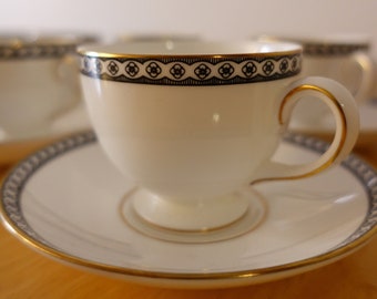 May include: A white teacup and saucer with a black and gold trim. The cup has a delicate floral pattern around the rim.