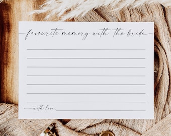 Op de afbeelding: Een witte kaart met de tekst "favourite memory with the bride" en gelijnde ruimtes om te schrijven. De kaart ligt op een houten oppervlak met een beige doek en decoratieve elementen, waaronder een gouden zegel en een gouden stempel.