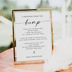 May include: A gold-framed sign with a white background and black text that reads "A message from the bump." The text continues with a message from the baby to the guests at a baby shower. The sign reads, "Thank you for being here for my mommy. It won't be long now till I come out of her tummy. I can't be there to thank you all, but I know my mommy loves you all! I know you all can't wait until I'm here, so make some memories today and hold them dear!" The sign ends with a heart symbol and the text "Baby Christopher."