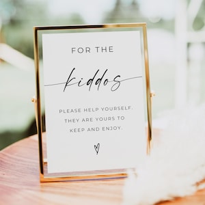 Puede incluir: Un cartel con marco dorado con el texto "FOR THE kiddos PLEASE HELP YOURSELF. THEY ARE YOURS TO KEEP AND ENJOY. ♡" sobre un fondo blanco.