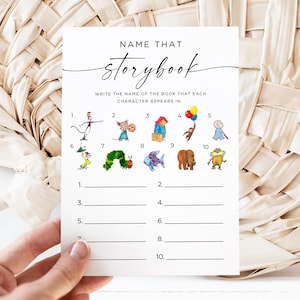 May include: A white card with the text "NAME THAT storybook" and illustrations of storybook characters. The card has numbered lines for answers. The card is held by a hand against a woven background.