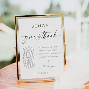 Könnte beinhalten: Ein Schild für ein Hochzeitsgästebuch mit goldenem Rahmen, auf dem die Worte "JENGA guestbook" stehen. Das Schild fordert die Gäste auf, ein Jenga-Teil mit guten Wünschen zu unterschreiben. Das Datum "06.14.202X" ist unten aufgedruckt.