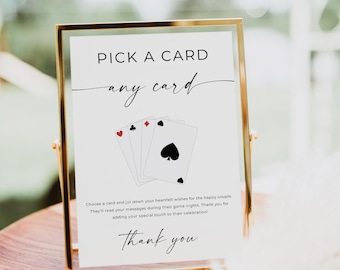 May include: A gold framed sign with the text "PICK A CARD any card" and three playing cards. The sign includes the text "Choose a card and jot down your heartfelt wishes for the happy couple. Thank you."