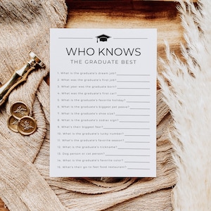 Op de afbeelding: Een spelkaart voor een afstudeerfeest met de tekst "WHO KNOWS THE GRADUATE BEST" en een afbeelding van een baret. De kaart bevat invulvragen over de voorkeuren en het leven van de afgestudeerde. De kaart ligt op een beige ondergrond met decoratieve elementen.