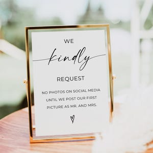 May include: A gold framed sign with the text "WE kindly REQUEST NO PHOTOS ON SOCIAL MEDIA UNTIL WE POST OUR FIRST PICTURE AS MR. AND MRS." A heart symbol is at the bottom.