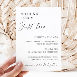 May include: A white rectangular wedding invitation card with black text that reads: NOTHING FANCY... Just love, CHRISSY + THOMAS, JOYFULLY INVITE TO THEIR INTIMATE WEDDING CELEBRATION, 08.21.202x, AT 5 O'CLOCK IN THE AFTERNOON, SUNRISE HIGHLAND CIRCLE HOTEL, SAN FRANCISCO, CALIFORNIA, dinner and drinks to follow.