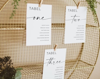 May include: A gold wire mesh display with three white cards clipped to it. Each card has the word "TABEL" and a number in black script. The cards list names. Greenery drapes over the top of the display, creating a decorative effect.