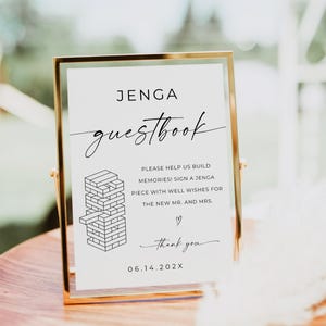Könnte beinhalten: Ein goldgerahmtes Schild mit der Aufschrift "JENGA guestbook". Der Text lädt dazu ein, ein Jenga-Teil mit Glückwünschen für das Brautpaar zu unterschreiben. Eine Jenga-Block-Illustration und "thank you" sind ebenfalls vorhanden. Das Datum 06.14.202X ist angegeben.